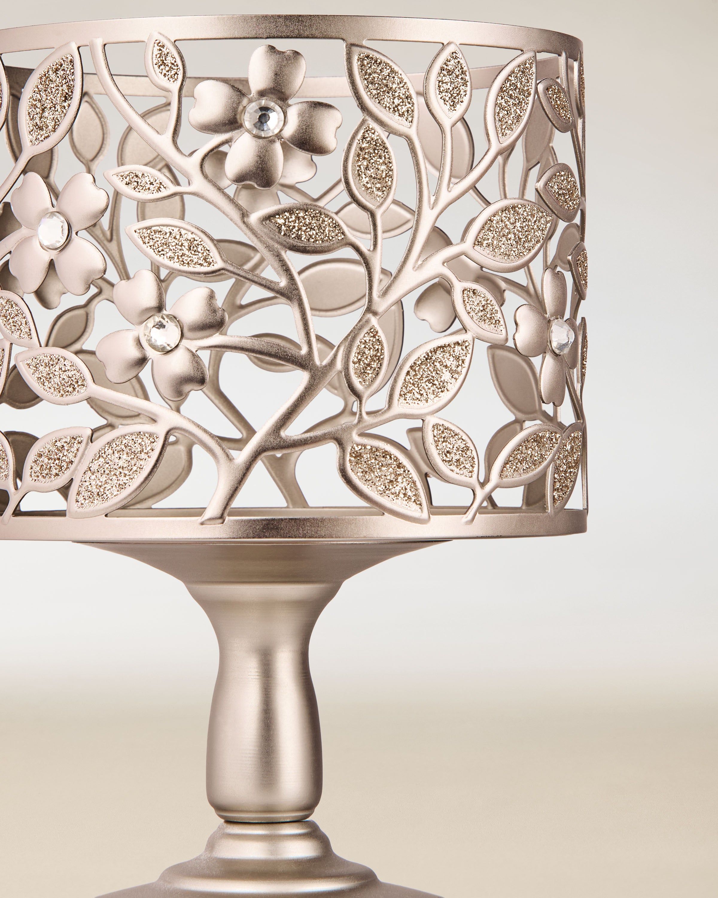 Metalowy świecznik na świece 3‑knotowe z ażurowym motywem liści i kwiatów, zdobiony delikatnym połyskiem i osadzony na stabilnej podstawie.