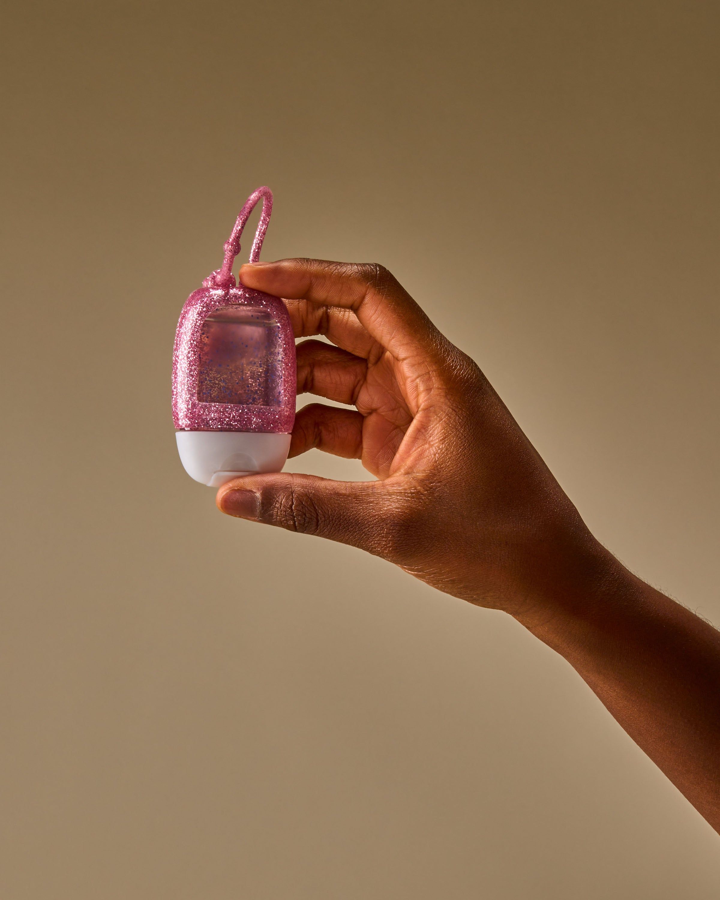 Ujęcie prezentujące brokatowy uchwyt PocketBac trzymany w dłoni, podkreślające jego kompaktową formę i elastyczną pętelkę do przypięcia.