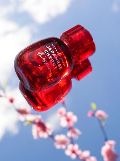 Czerwona woda perfumowana Bath & Body Works Japanese Cherry Blossom na tle nieba i kwiatów