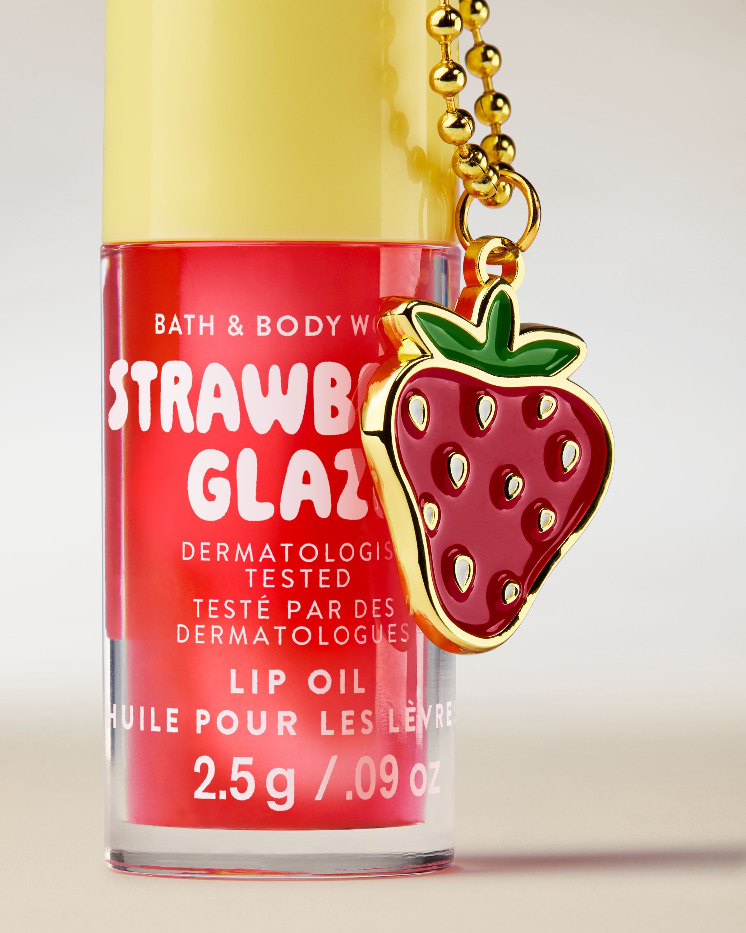 Olejek do ust Bath & Body Works Strawberry Glaze 2,5 g w różowym opakowaniu z brelokiem w kształcie truskawki.