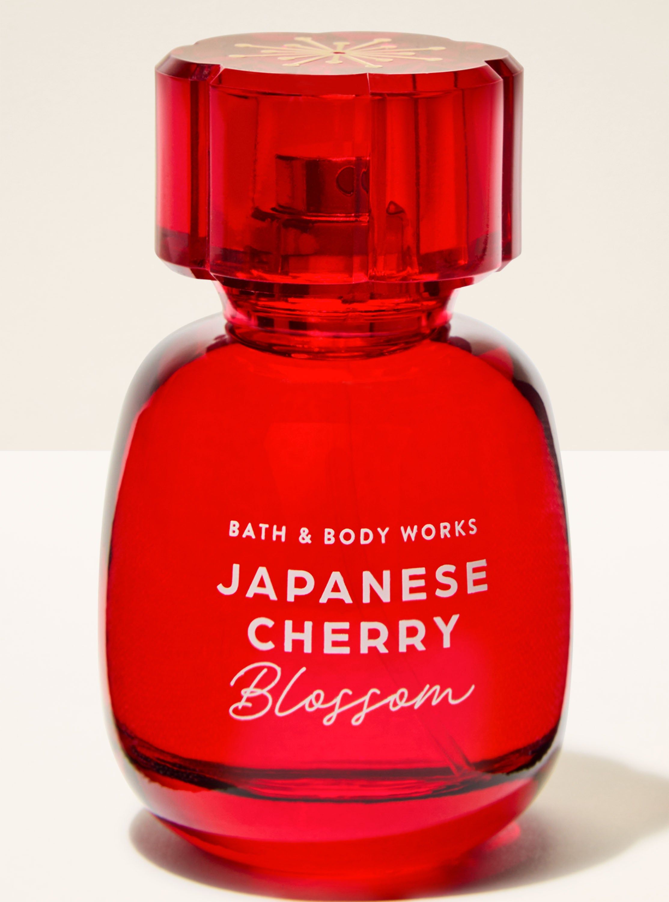 Czerwona woda perfumowana Bath & Body Works Japanese Cherry Blossom na tle nieba i kwiatów