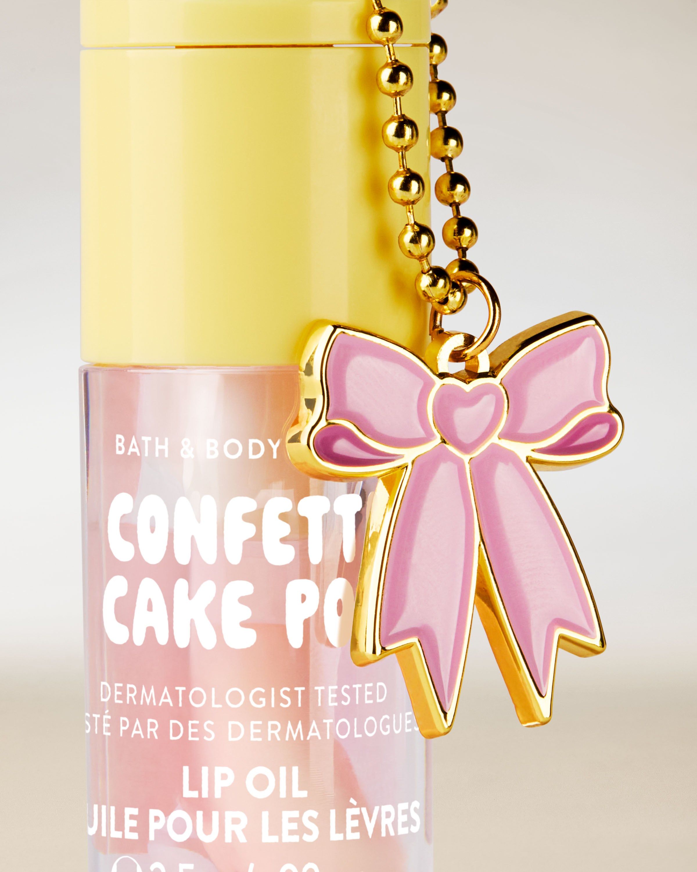 Olejek do ust Bath & Body Works Confetti Cake Pop 2,5 g w pastelowym opakowaniu z brelokiem w kształcie kokardy.